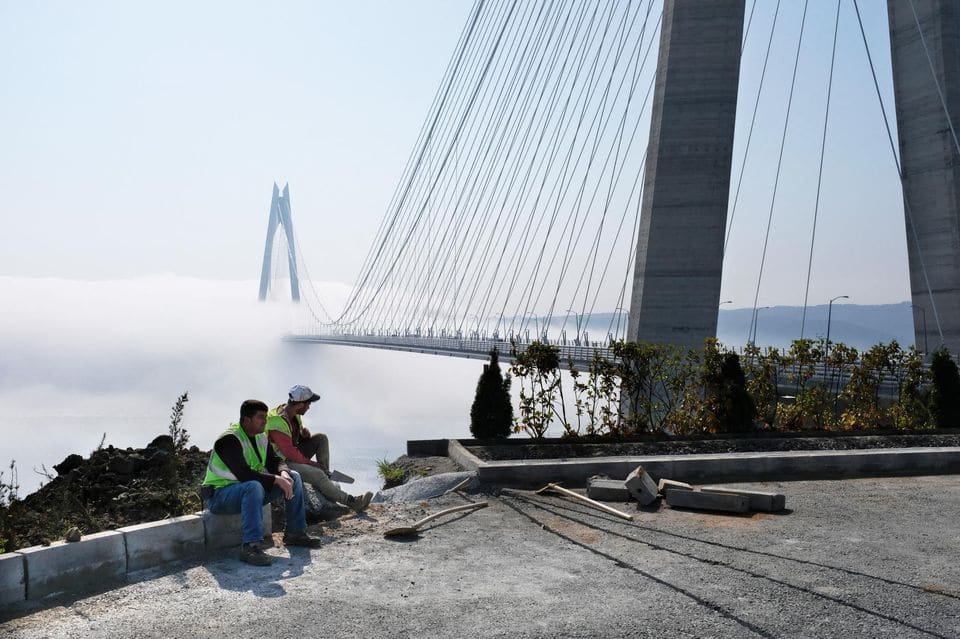 Deux hommes sont assis au bord d'un pont dans le brouillard, réfléchissant à l'opportunité de boycotter ou non les produits américains en Turquie.