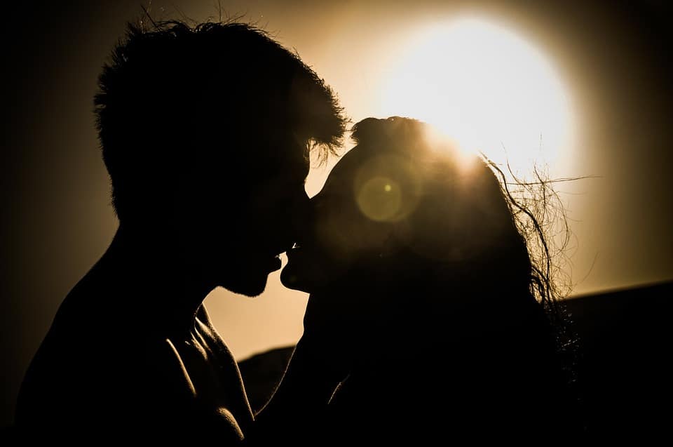 Un couple passionné partageant un tendre baiser sur fond de coucher de soleil vibrant.