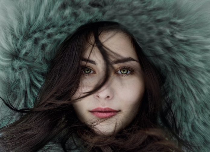 Une femme vêtue d'un manteau de fourrure vert pose pour une photo, présentant l'une des 5 manières de trouver l'inspiration mode pour cet hiver.
