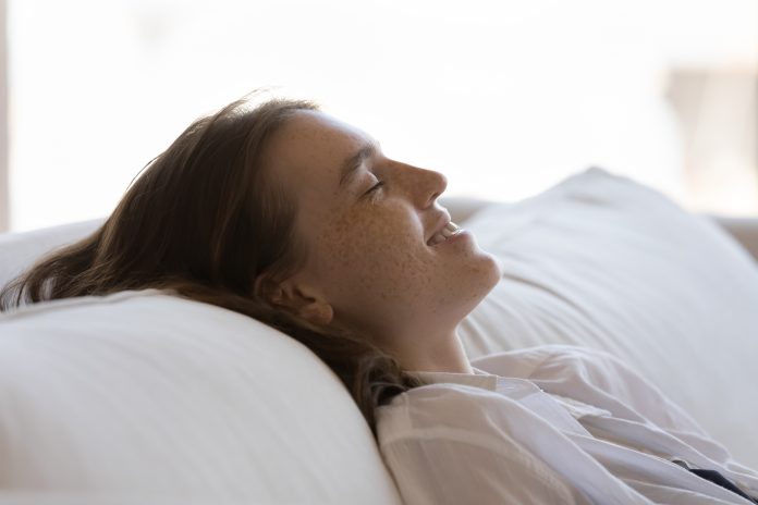 Une femme paisiblement allongée sur un canapé blanc, les yeux fermés, profitant d'un moment de détente.
