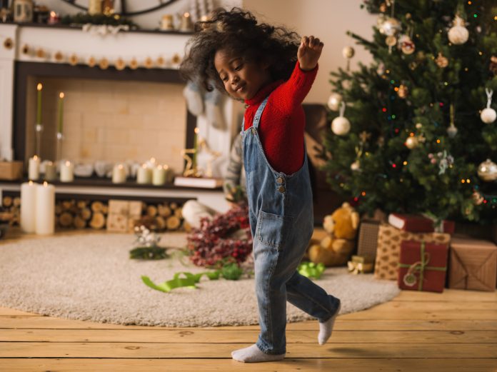 Profiter des fêtes avec une petite fille dansant devant un sapin de Noël.