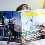 Une femme lit un magazine Ikea sur un canapé, entourée de trésors cachés et de meubles anciens.