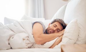 Un homme dort dans un lit avec des draps blancs.