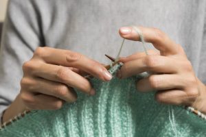 Les mains d'une femme tiennent une aiguille à tricoter pendant qu'elle tricote un pull en laine.