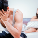 Un homme est assis sur un lit, les mains sur le visage en état de brouillon.