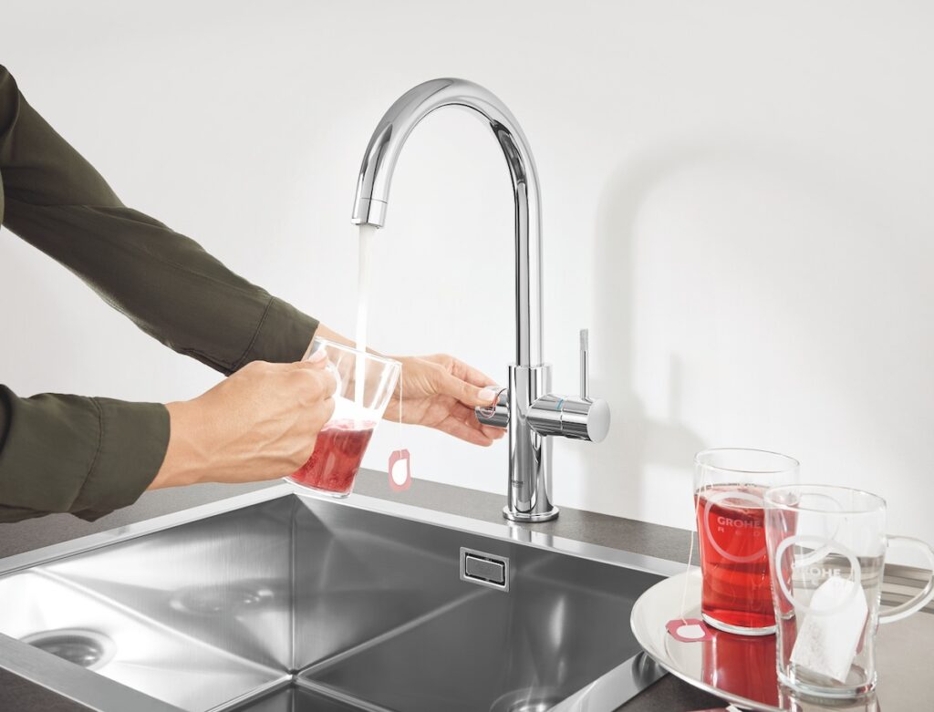 Une femme verse un verre de vin rouge dans un évier tout en faisant la vaisselle.