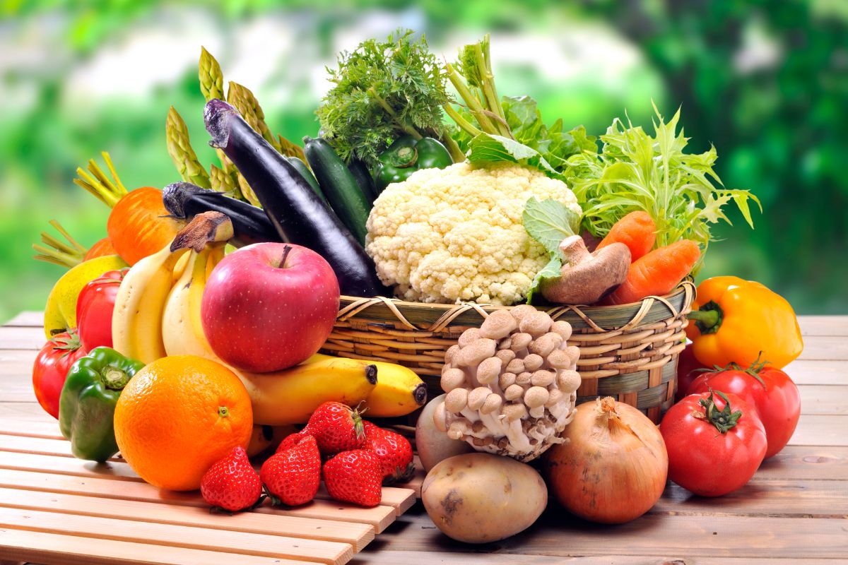 Assortiment de fruits et légumes frais, clé de l'alimentation anti-âge, présentés dans un panier sur une surface en bois avec un fond vert flou.