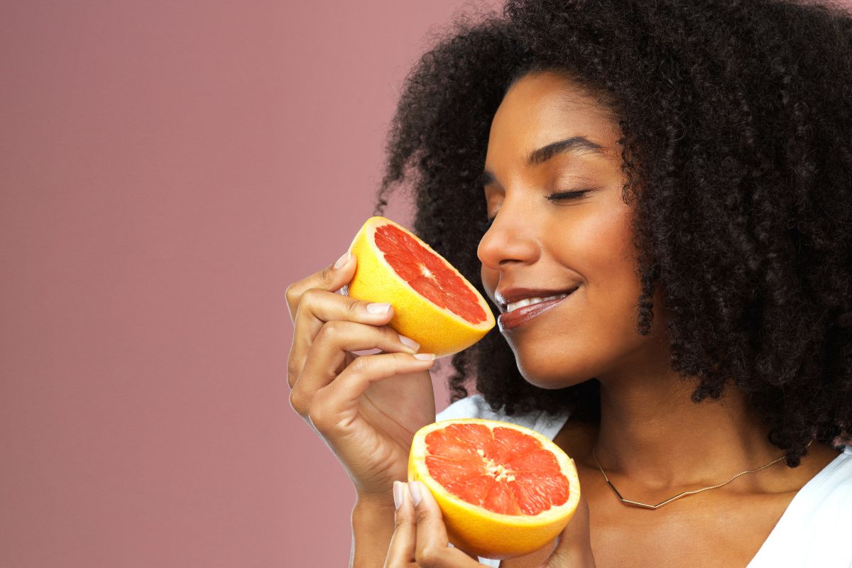 Une femme souriante et tenant une tranche de pamplemousse jusqu'à son nez, dévoilant ses préférences alimentaires.