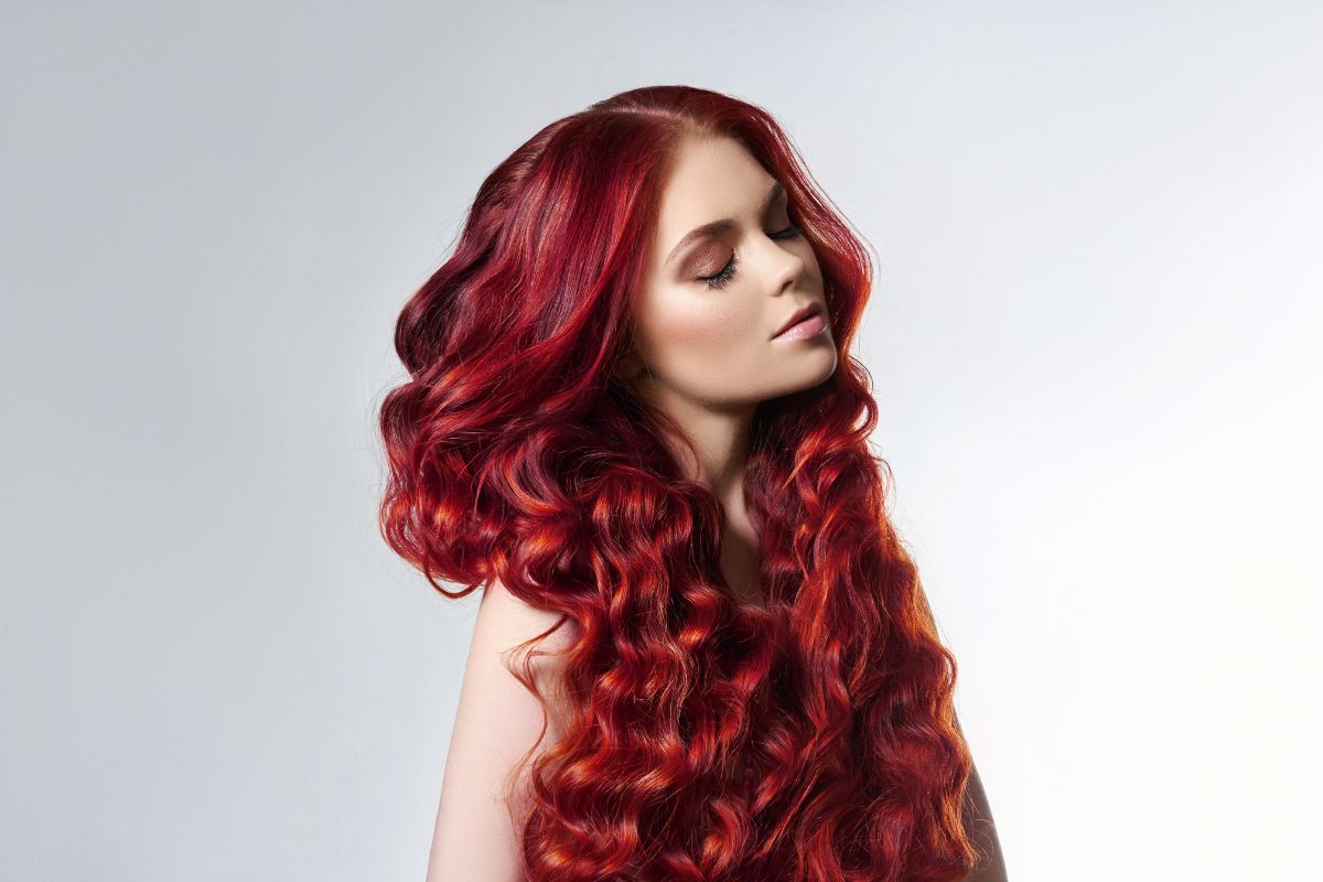 Une femme aux longs cheveux roux ondulés présentant les dernières tendances en matière de coloration sur un fond gris clair.