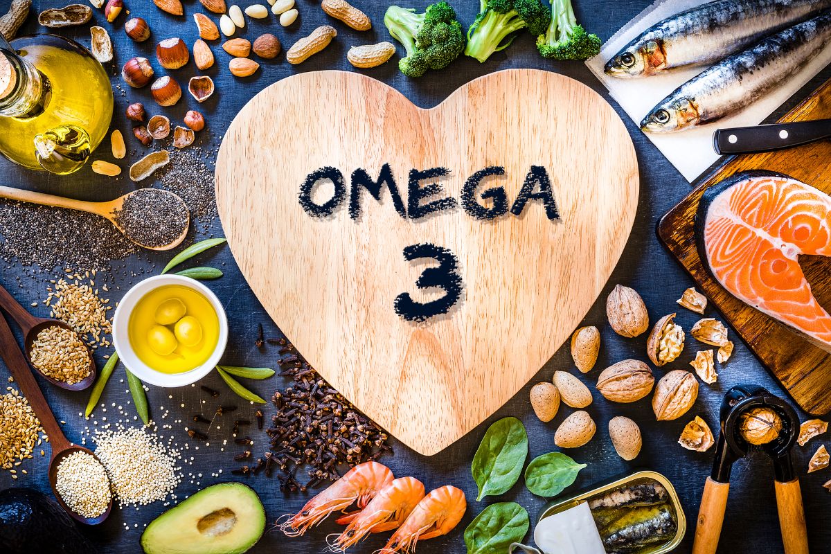 Divers aliments riches en oméga-3 comme le poisson, les noix, les graines et les huiles présentés autour d'un cœur en bois sur lequel est écrit « Dompter la ménopause ».