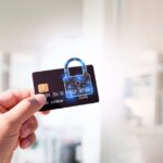 Gros plan d'une main tenant une carte de crédit surmontée du symbole du cadenas holographique de Brouillon Auto, indiquant la sécurité. L’arrière-plan est flou, avec un décor intérieur de couleur claire.