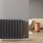 Radiateur noir fixé à un mur gris clair dans un espace de vie moderne avec un plancher en bois à chevrons, un piédestal orange et un buffet beige à thème automobile en arrière-plan.