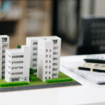 Maquettes de bâtiments sur un bureau avec des documents, un ordinateur portable et des billets de banque, reflétant la scène immobilière animée en Île-de-France.