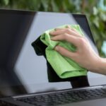 En nettoyant délicatement l'écran d'ordinateur avec un chiffon en microfibre vert, une plante floue ajoute une toile de fond sereine à ce guide pratique.