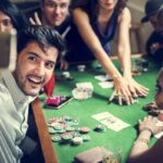 Un groupe de streamers de casino joue au poker à une table verte. Une personne au premier plan prend un selfie. Des jetons de poker, des cartes et des boissons sont sur la table, capturant l'essence du divertissement en ligne moderne.