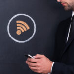 Un homme en costume se tient devant un tableau noir avec un symbole Wi-Fi, démontrant la fonction Brouillon Auto sur son smartphone.
