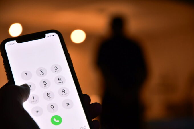 Une main tenant un smartphone avec un écran de numérotation, comme un brouillon automatique capturant l'instant, tandis que la silhouette floue d'une personne s'attarde en arrière-plan.