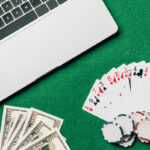 Un ordinateur portable repose sur une table verte au milieu d'un brouillon de cartes à jouer éparpillées, de jetons de poker et de billets de dollars.
