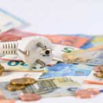 Une prise électrique repose sur une pile de billets et de pièces en euros, faisant écho au brouillon automatique du calcul de la hausse des coûts de l'énergie.