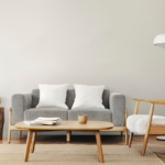 Un salon moderne avec un canapé gris, des coussins blancs et une table basse en bois illustre la créativité. Il comprend une chaise simple, une table d'appoint avec une plante et un lampadaire élégant, créant des espaces uniques.