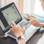 Une personne tape sur un ordinateur portable, avec des messages et des documents ouverts à côté d'un convertisseur en ligne gratuit. Une plante en pot et un cahier sont posés sur le bureau, favorisant un espace de travail serein.
