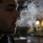 Un homme exhale de la fumée sur un arrière-plan flou à l'intérieur.