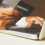 Une personne tient une carte de crédit dans une main et tape sur un clavier d'ordinateur portable avec l'autre, soulignant la facilité de faire des achats en ligne ou d'utiliser des cartes-cadeaux numériques, comme celles proposées par le CSE d'entreprises.