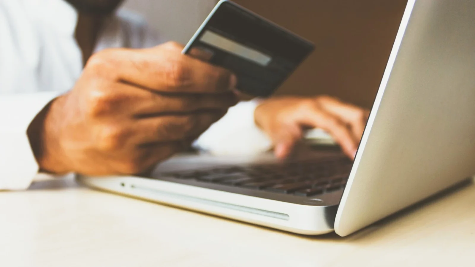 Une personne tient une carte de crédit dans une main et tape sur un clavier d'ordinateur portable avec l'autre, soulignant la facilité de faire des achats en ligne ou d'utiliser des cartes-cadeaux numériques, comme celles proposées par le CSE d'entreprises.