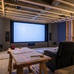 Home cinéma en cours d'aménagement : ossature bois apparente, sol brut et grand écran avec fauteuils de cinéma ; outils et plans disposés sur une table, prêts pour des soirées streaming inoubliables.