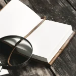 Open blank notebook with a leather cover and a string bookmark on a dark wooden desk.