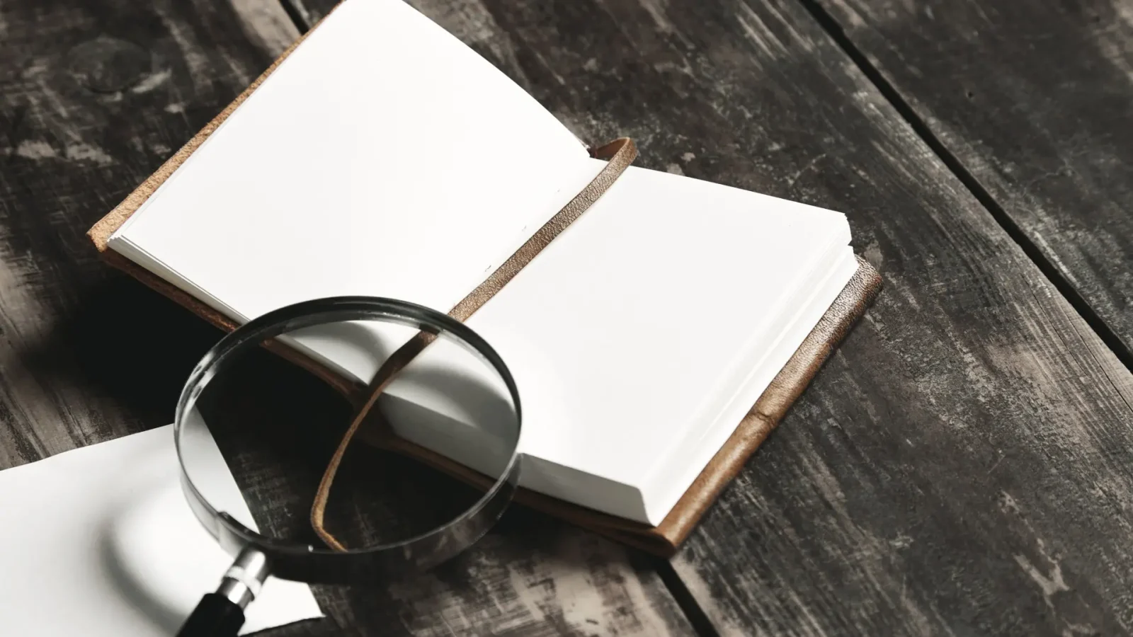 Open blank notebook with a leather cover and a string bookmark on a dark wooden desk.
