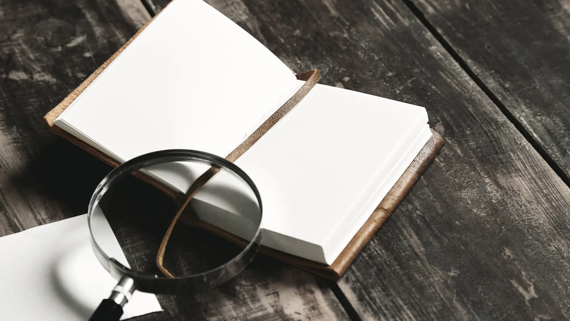 Open blank notebook with a leather cover and a string bookmark on a dark wooden desk.