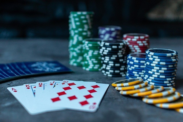 Des cartes à jouer et des piles de jetons de poker colorés sont disposés sur une table, avec une quinte flush royale à carreaux bien en évidence au premier plan.